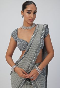 This exquisite Grey Crystal and Sequin Embroidered Georgette Saree radiates sophistication and charm, crafted from luxurious georgette fabric. The pre-draped grey saree is meticulously hand-embroidered with sparkling sequins and crystal accents, creating a mesmerizing, head-turning effect. Paired with a stylish cap-sleeve blouse adorned with dazzling crystal details, this set seamlessly blends modern flair with timeless elegance. Ideal pre draped choice for weddings, receptions, or festive celebrations. Composition : Saree, Blouse - Georgette Care: Dry Clean Only and Vacuum Storage This product can be customized for sleeves, blouse length and neckline Delivery : 6-8 weeks as the product is hand crafted. Check Size Guide or choose MySize for free customisation (All Sizes above XL can be mad Cap Sleeves Blouse Saree, Grey Saree Look, Vani Vats, Grey Saree, Crystal Embroidery, Weddings Receptions, Ethnic Chic, Stylish Caps, Vacuum Storage