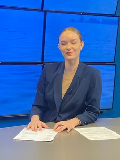 a woman sitting at a table with papers in front of her on the news desk