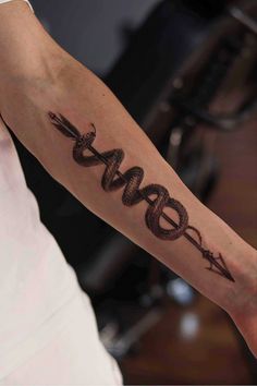 a woman's arm with a snake and arrow tattoo on her left arm,