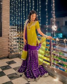 a woman in a yellow and purple dress standing on a balcony with lights strung from the ceiling