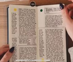 two hands holding an open book on top of a wooden table