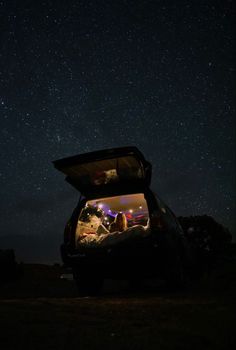 the back end of a car with its trunk open and people sitting in it at night