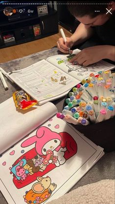 a young boy sitting at a table with lots of coloring books and markers in front of him