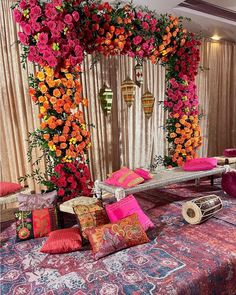 a bed covered in pink and orange pillows next to a wall with flowers on it