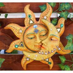 a yellow sun face sitting on top of a wooden wall next to green ivys