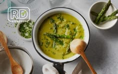 a white bowl filled with broccoli soup next to other bowls and spoons