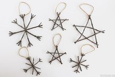 four snowflakes made out of twigs are hanging from twine strings on a white surface