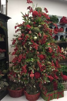 a christmas tree with red berries and greenery in baskets on the floor next to shelves