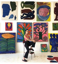 a woman sitting on a chair in front of many colorful paintings and artwork hanging on the wall