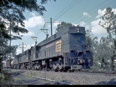 an old train is traveling down the railroad tracks near some trees and power lines on a sunny day