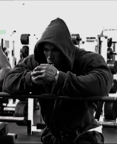 a man sitting in front of a barbell with his hands on his chest and looking at his cell phone