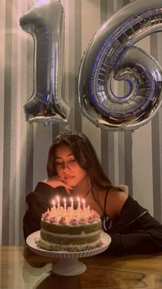 a woman sitting in front of a cake with candles on it and the number six behind her