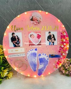 an illuminated sign with baby's feet and pictures on it, surrounded by flowers