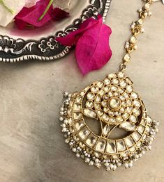 a gold necklace with pearls hanging from it's side next to a pink flower