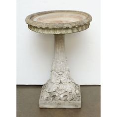 a birdbath sitting on top of a cement floor next to a white wall