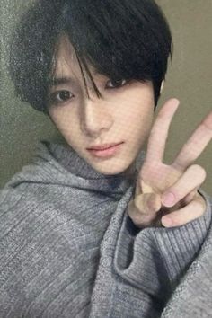 a young man making the v sign with his hand while wearing a gray sweater and scarf