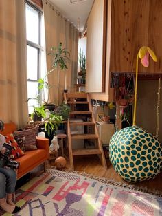 a woman sitting on an orange couch in a living room next to a tall window