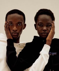 two young men sitting next to each other in front of a white wall with their hands on their faces