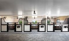 the inside of a horse stable with white and black stalls on each side, doors open to let in plenty of light