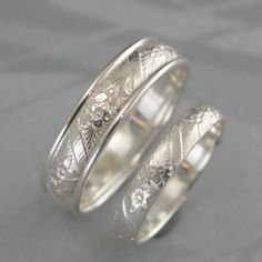 two wedding bands with engraved designs on them, one is white gold and the other is silver