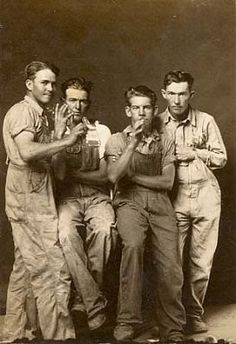 an old black and white photo of four men in overalls posing for the camera