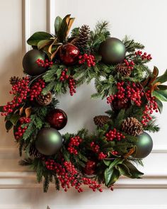 a christmas wreath with red berries, green and gold baubs on it is hanging from the wall