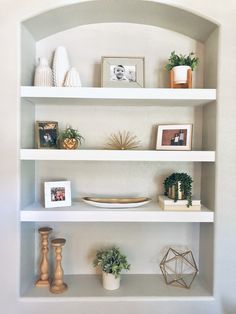 some white shelves with plants and pictures on them