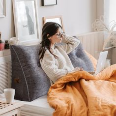 a woman sitting on a bed using a laptop computer while holding her hand up to her ear