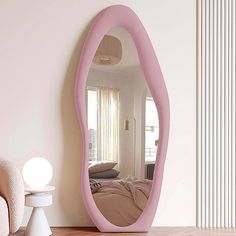 a large pink mirror sitting on top of a wooden floor next to a white chair