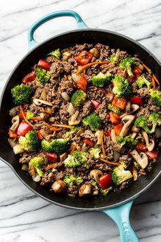 a skillet filled with ground beef, broccoli and mushrooms