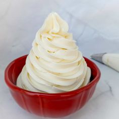 a red bowl filled with whipped cream next to a knife