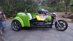 a man standing next to a green motorcycle with side car in the street near trees