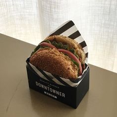 a close up of a sandwich in a box on a table with a window behind it