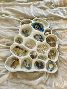 a white tray filled with lots of different types of jewelry on top of a bed