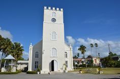 a white church with a clock on the front and side of it, surrounded by palm trees