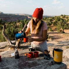 a woman sitting on top of a rock next to a cup