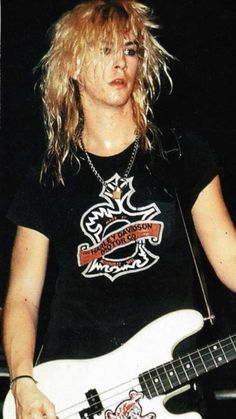 a woman with blonde hair holding a white guitar in front of a microphone and wearing a black t - shirt