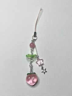 a pair of earrings with charms attached to them on a white surface, one is pink and the other is green