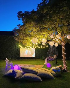 an outdoor movie is set up in the yard with pillows and lights around it,