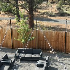 an outdoor seating area is set up with lights strung across the fence and trees in the background