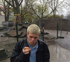 a man standing in front of a fence with his hand on his fist and looking down at the ground