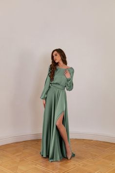 a woman in a long green dress standing on a wooden floor with her legs crossed