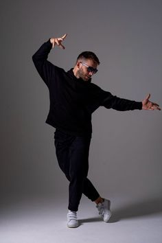 a man in black shirt and sunglasses doing a dance move with his arms out to the side