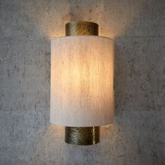 a wall light with a white shade on it's side against a concrete wall