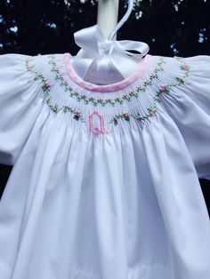 a white smock with pink trim and embroidered letters