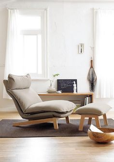 a chair and ottoman in front of a window with a vase on the floor next to it