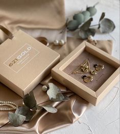 two boxes with jewelry sitting on top of a satin table cloth next to some flowers