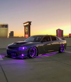 a black car with purple wheels parked in front of a building at sunset or dawn