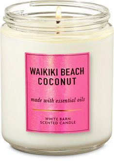 a white candle with pink label sitting in front of a white background that says waiki beach coconut