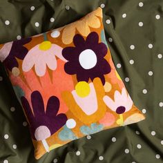 an orange and purple flowered pillow sitting on top of a green bed sheet with white polka dots